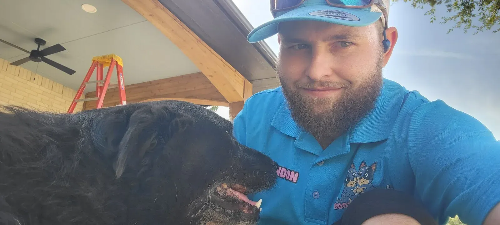 Brandon on a covered patio with a customer's shaggy black dog
