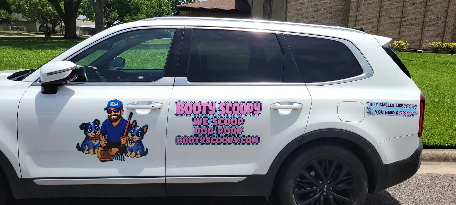 The white Booty Scoopy SUV with its pink and blue We Scoop Dog Poop lettering